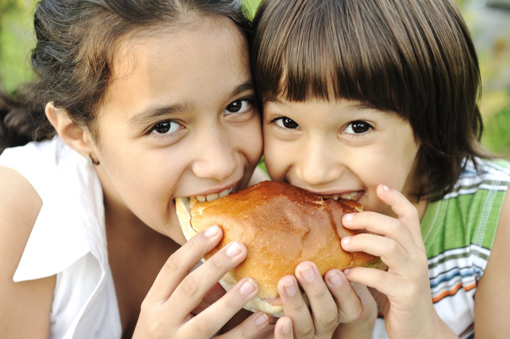 Closeup of two children eating sandwich in nature together, healthy food, care and love